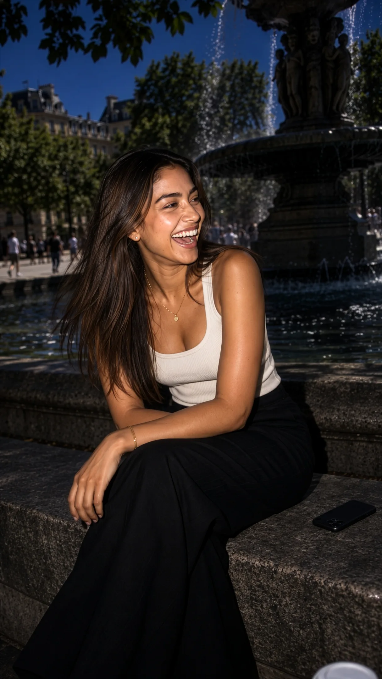A creator mid-laugh on the rim of a plaza fountain at midday, phone face-down beside her coffee.