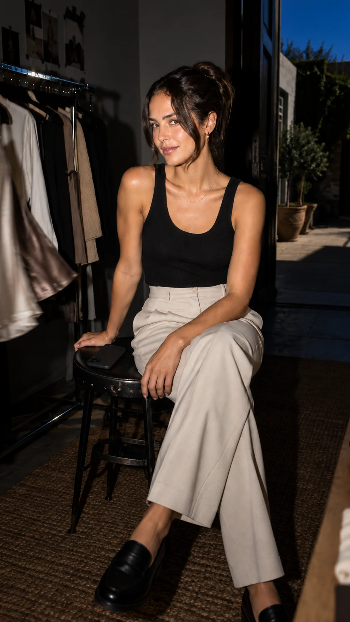 A founder on a showroom stool, phone face-down — the DMs are being answered from her catalog.