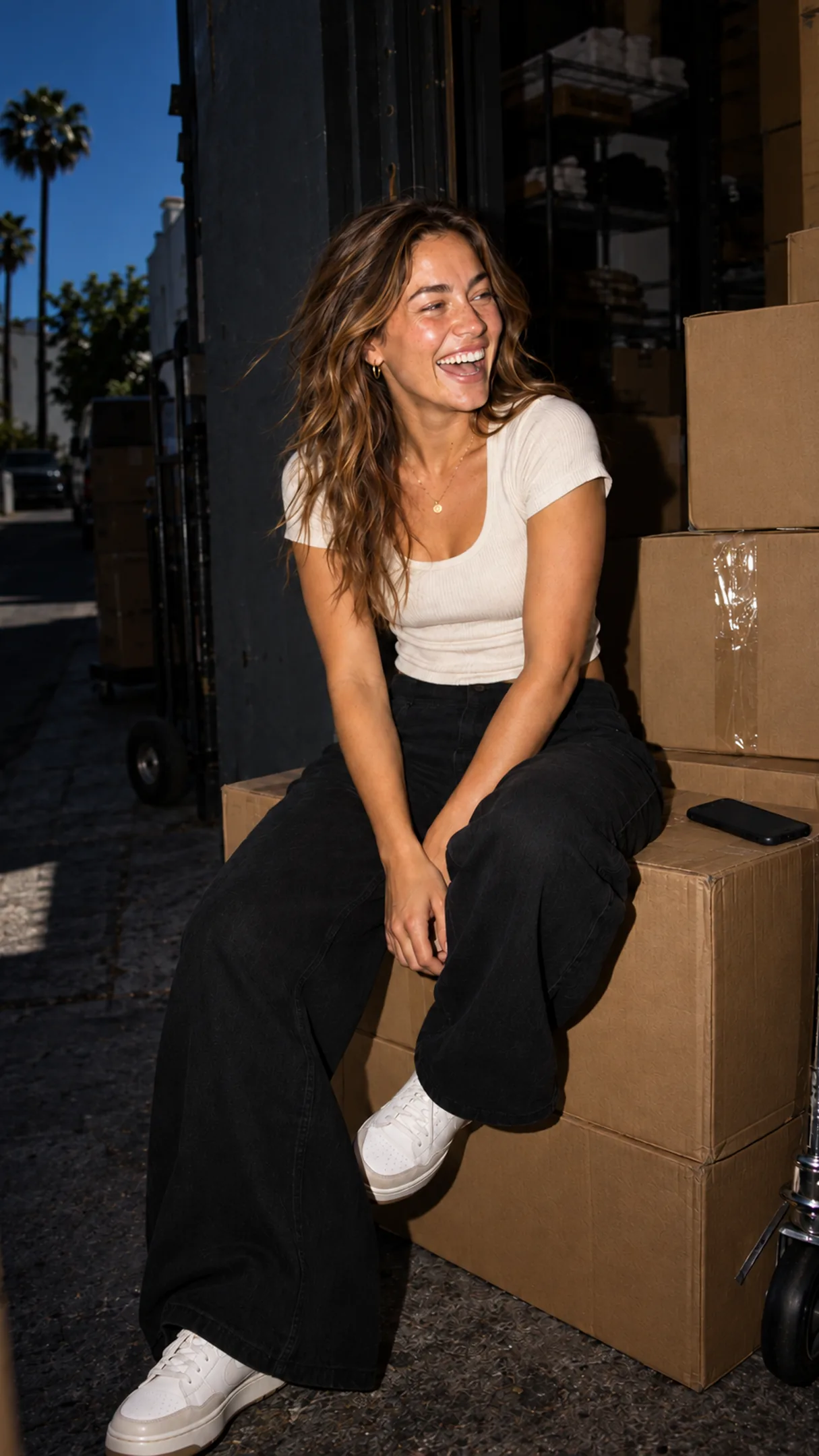 A creator laughing on a stockroom box, phone face-down — the restock note already out to the right list.